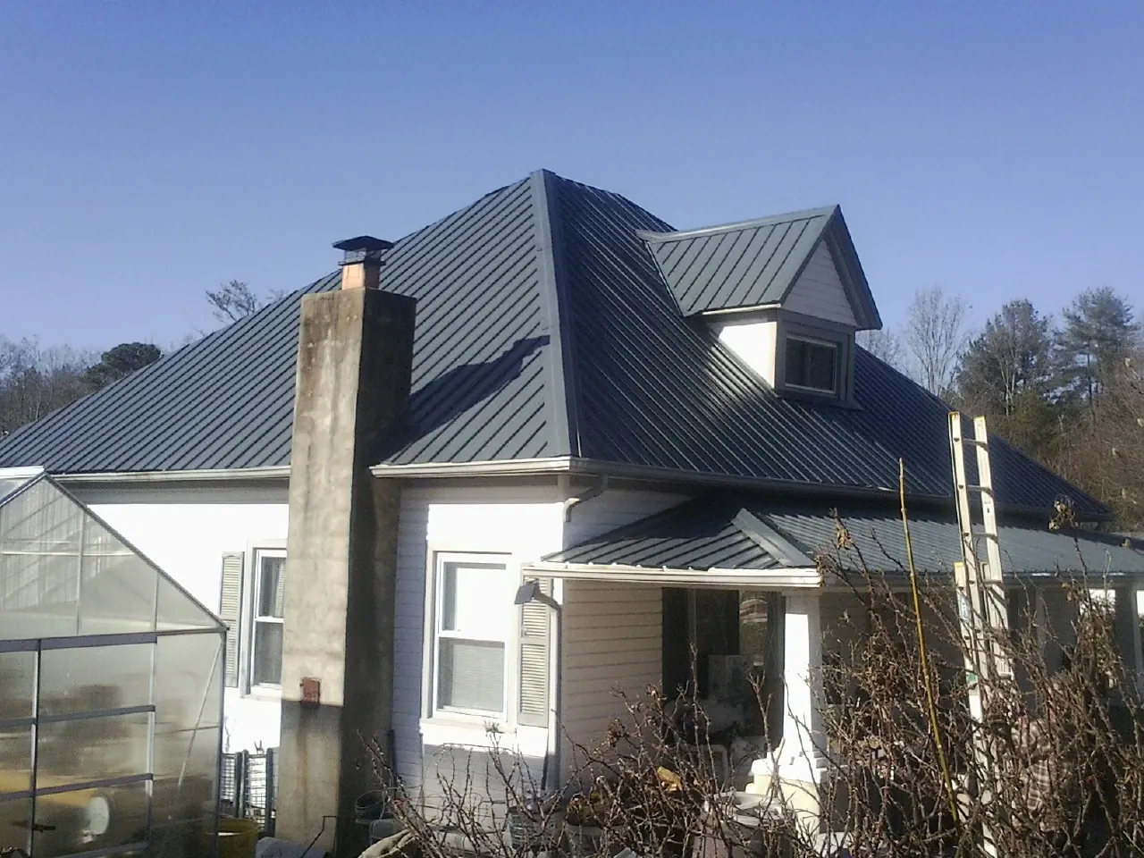 Dark blue standing seam metal roof on a white farmhouse with dormer — Slate & Tile Roof Repair by Roofing Brothers in Custar