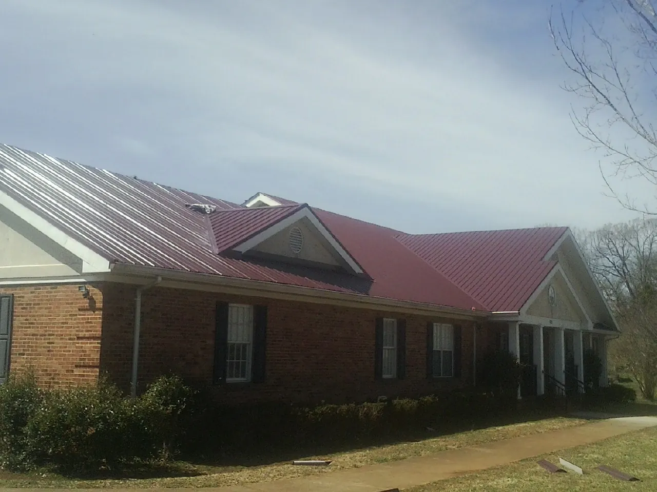 Red metal roof with gabled entries on a long brick building, from a Hail Damage Roof Repair job in Custar