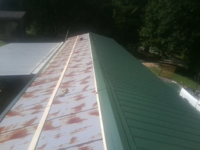 Old rusted panels beside newly installed green metal roofing — Wind Damage Roof Repair by Roofing Brothers in Custar