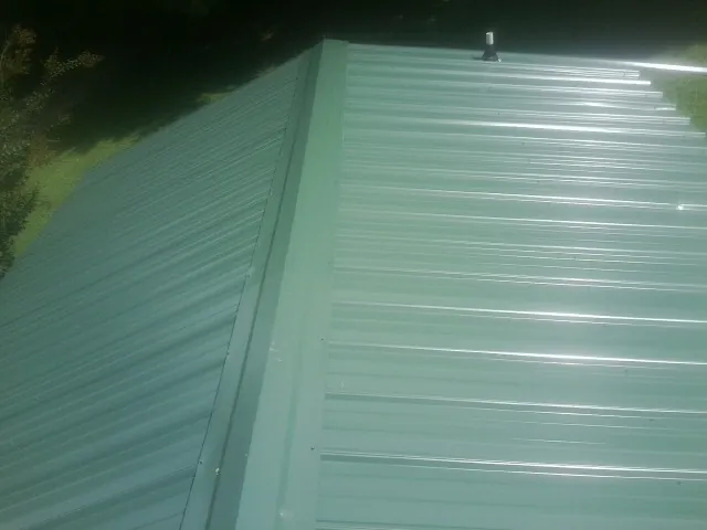 New green metal panels meeting at the ridge of a roof — Flat Roof Repair work by our crew in Custar