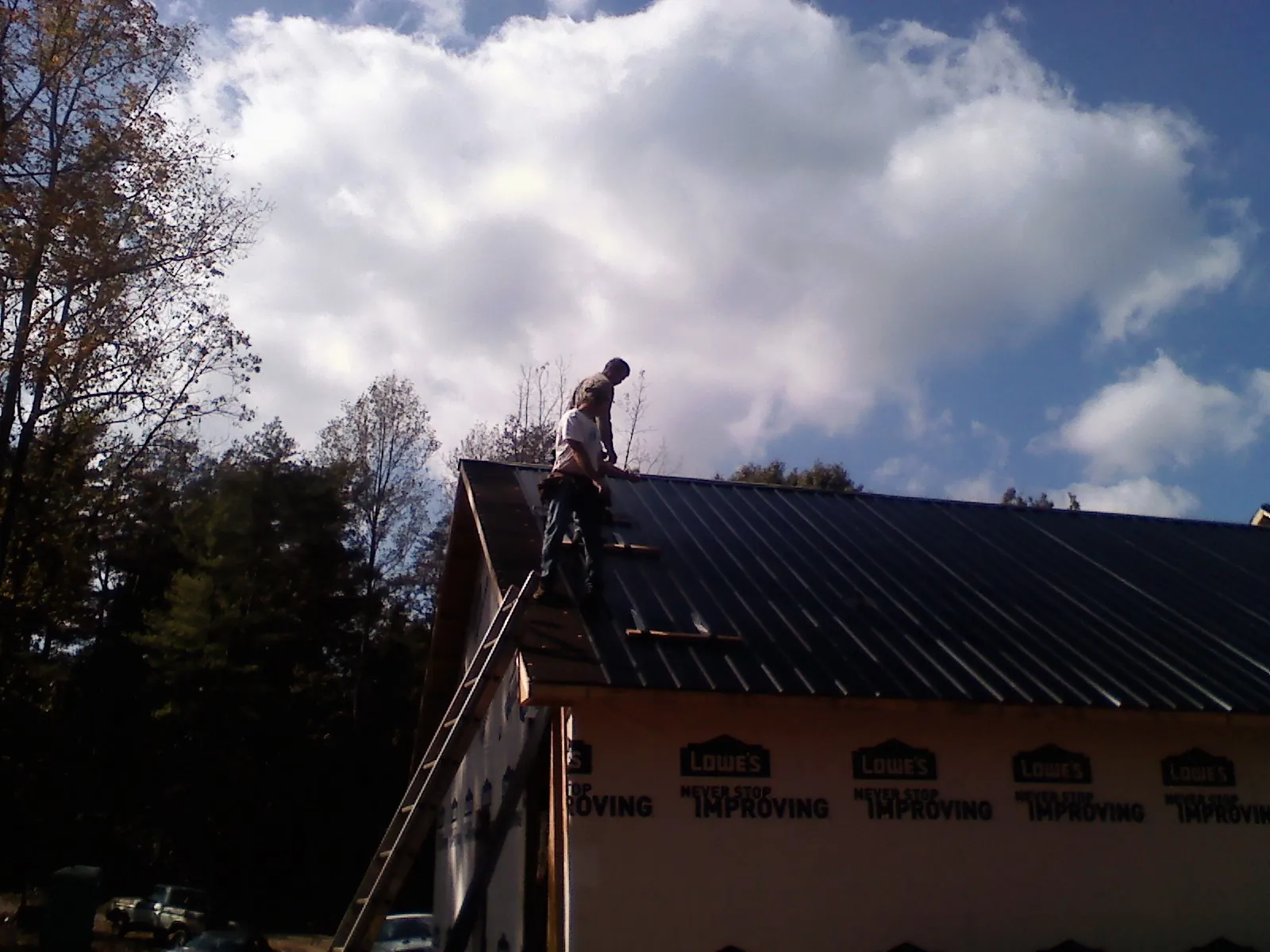 Roofer fastening dark metal panels high against a cloudy sky, from a Roof Inspection job in Custar